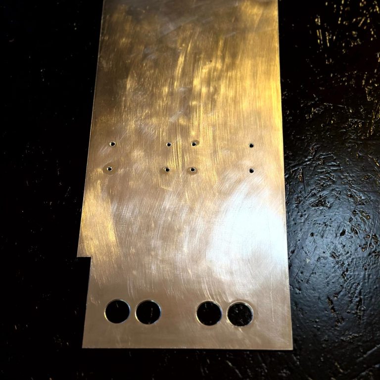 Eine metallene Platte mit mehreren Bohrlöchern und einer glänzenden Oberfläche. Bereit für die Weiterverarbeitung im Kühlkreislauf. 